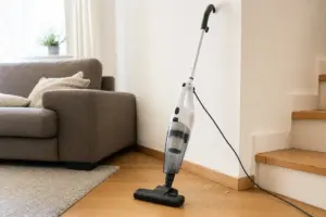 Aspirapolvere a scopa 2 in 1 con cavo appoggiato al muro vicino alle scale, con briciole sul pavimento