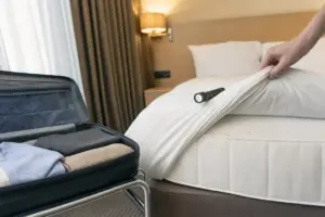 Valigia aperta su portabagagli e controllo del materasso in una camera d’hotel con torcia e piccole macchie