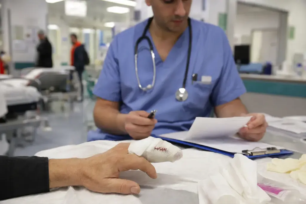 Medico in pronto soccorso controlla documenti mentre una mano del paziente con dito fasciato e suturato riposa sul lettino