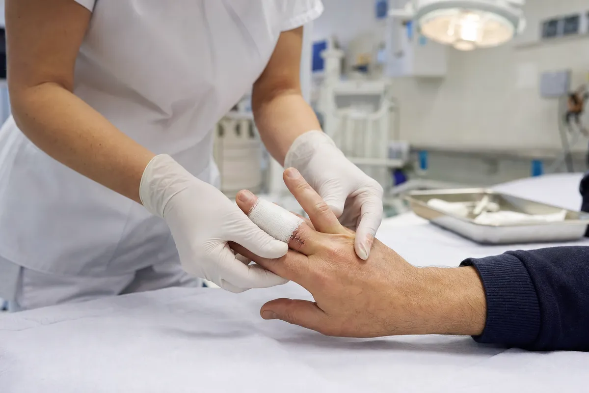 Operatore sanitario con guanti esamina un dito della mano con fascia e punti di sutura su lettino medico