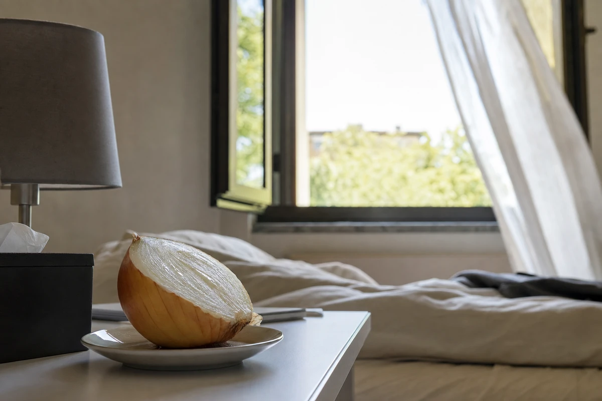 Mezza cipolla su un piattino sul comodino, con finestra aperta e tenda leggera in una camera da letto