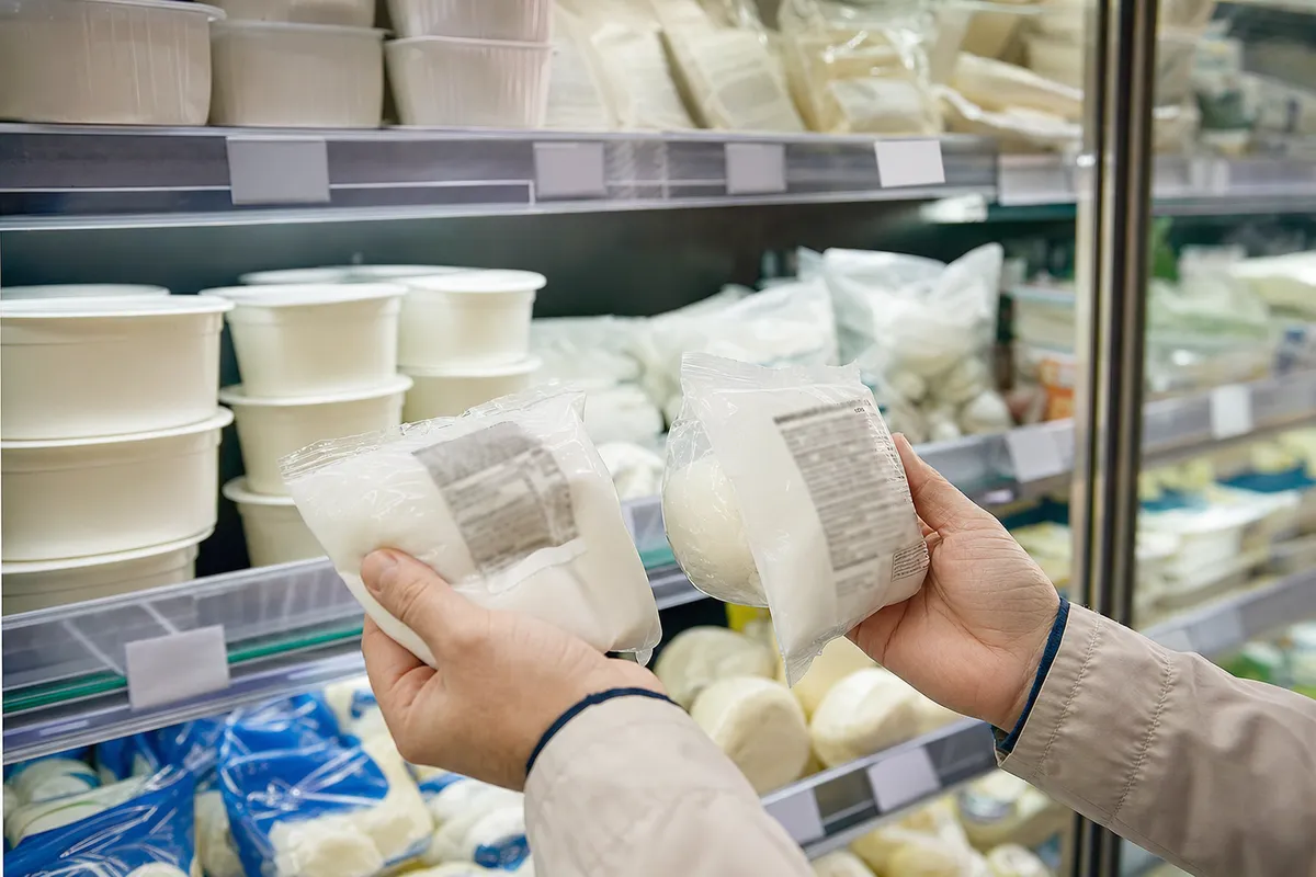 Mani di un cliente confrontano due confezioni di mozzarella davanti allo scaffale frigo del supermercato