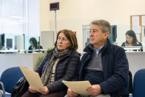 Donna e uomo seduti in sala d’attesa di un ufficio, con cartelle di documenti in mano