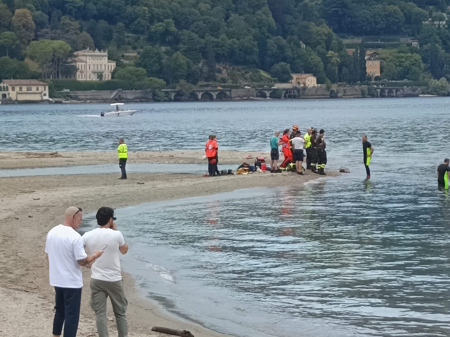 Una spiaggia del lago con cartelli di divieto e persone che si avvicinano, con amministratori che osservano