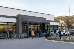 Ingresso di un negozio discount con vetrate, file di carrelli e clienti all’entrata, parcheggio sullo sfondo