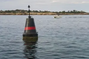 Boa di navigazione nera con banda rossa in mare calmo, con una barca a motore sullo sfondo