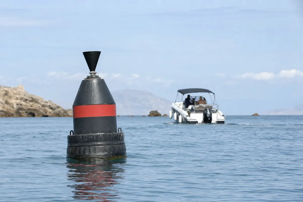 Boa di segnalazione nera con banda rossa in primo piano, con motoscafo sullo sfondo in mare calmo