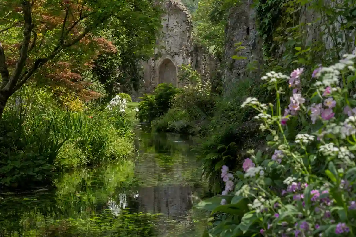 Ruscello limpido tra fiori e vegetazione primaverile, con rovine in pietra sullo sfondo nel Giardino di Ninfa