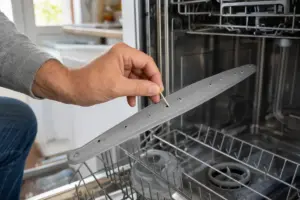 Mano che pulisce con uno stuzzicadenti i fori del braccio spruzzatore nella lavastoviglie aperta