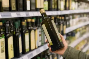 Mano che tiene una bottiglia di olio extravergine davanti allo scaffale del supermercato