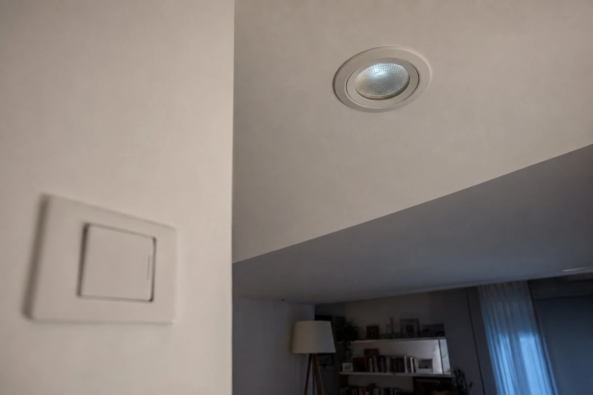 Faretto LED a incasso sul soffitto con lieve bagliore, interruttore a parete sfocato in primo piano