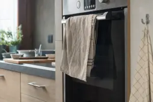 Strofinaccio beige appeso alla maniglia del forno in una cucina moderna, con lavello e piano lavoro sullo sfondo