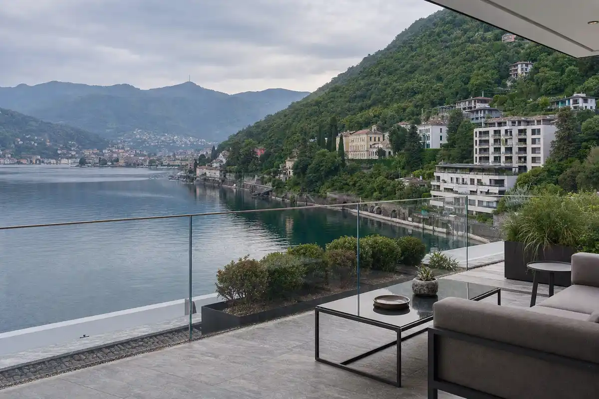 Terrazza di un appartamento moderno con vista su un lago, colline verdi e palazzi lungo la riva