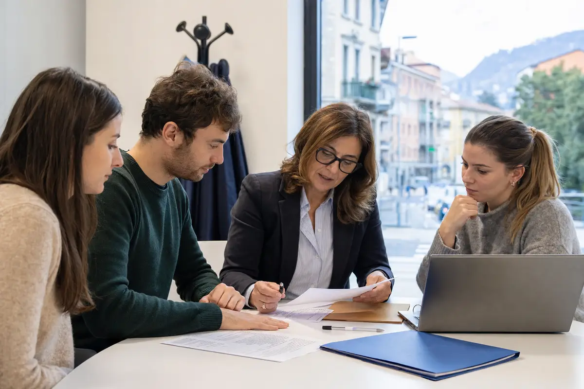 Consulente del lavoro con due giovani che esaminano CV e documenti su un tavolo, con laptop e cartelline