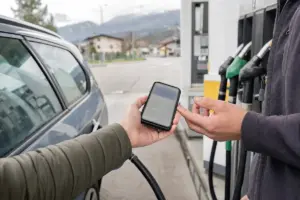 Mano che mostra uno smartphone a un addetto alla pompa di benzina accanto a un’auto in una stazione di servizio