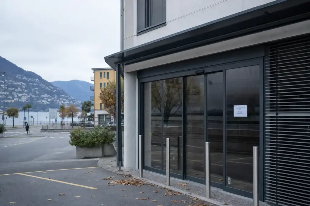 Ingresso di un supermercato chiuso con cartello “Chiuso domenica”, davanti a un parcheggio vuoto e un lago sullo sfondo