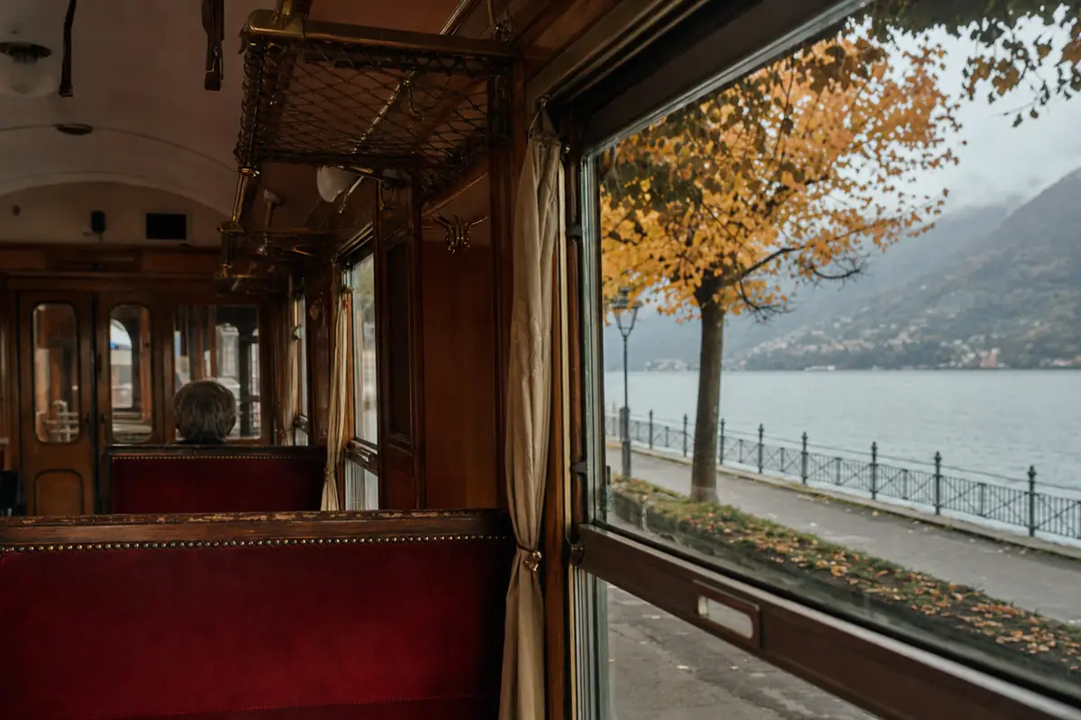 Interno di carrozza d’epoca con sedili in velluto rosso e vista sul lago e alberi autunnali dal finestrino