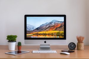 PHATTHALUNG, THAILAND - MARCH 24, 2018: iMac computers, iPhone, iPad, plant vase, cactus, pencils  and clock on wooden table, created by Apple Inc.