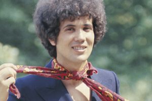 Il cantautore italiano Lucio Battisti si allaccia sorridente un foulard al collo. 1969