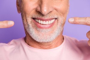 Cropped photo of retired old man face mouth direct fingers white shiny teeth wear pink t-shirt isolated violet color background.