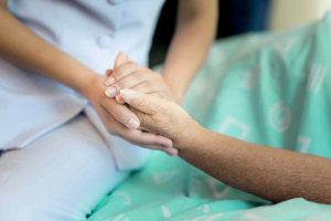 Nurse sitting on a hospital bed next to an older woman helping hands, care for the elderly concept