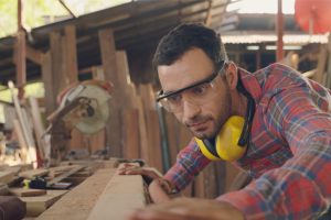 Carpenter caucasian young check quality the wood specification in furniture design in the factory. Wearing safety Mechanic Mask while working. Product quality inspection service.