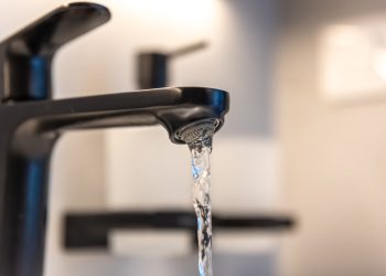 Macro of a black faucet aerator with a ribbon of water. Focus on metal texture and cleanliness for a modern bathroom.