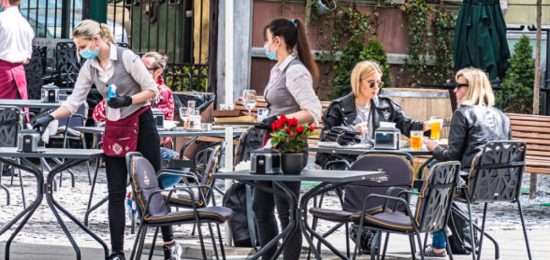 Vilnius, Lithuania - May 3 2020: Waitresses with a mask and gloves disinfecting the table of an outdoor bar, café or restaurant with blonde girls at the table, reopening after quarantine restrictions
