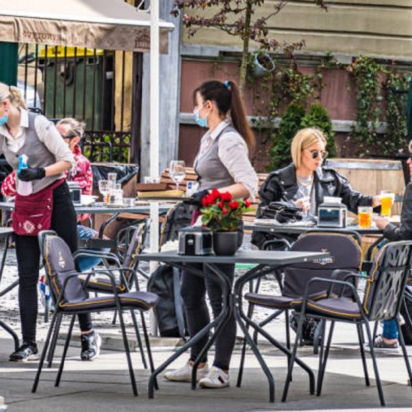 Vilnius, Lithuania - May 3 2020: Waitresses with a mask and gloves disinfecting the table of an outdoor bar, café or restaurant with blonde girls at the table, reopening after quarantine restrictions