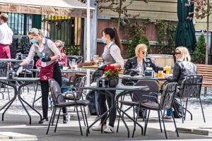 Vilnius, Lithuania - May 3 2020: Waitresses with a mask and gloves disinfecting the table of an outdoor bar, café or restaurant with blonde girls at the table, reopening after quarantine restrictions
