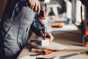 A man carves a tree. The carpenter works with a drill in a studio. An engineer provides a tree shape