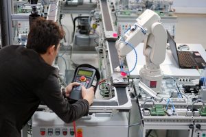 Man is working to control a robotic arm which is integrated on smart factory production line. industry 4.0 automation line which is equipped with sensors and robotic arm. Selective Focus.
