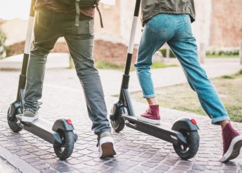Close up of people couple using electric scooter in city park - Millenial students riding new modern ecological mean of transport - Green eco energy concept with zero emission - Warm sunshine filter