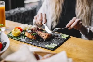 a woman eating baked fish fillet with herbs and vegetables at the table