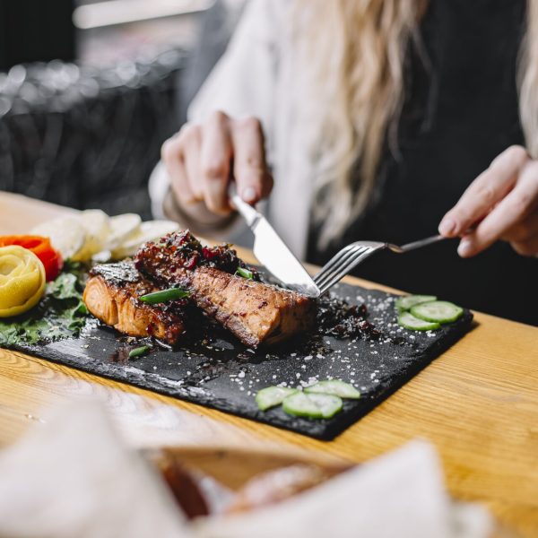 a woman eating baked fish fillet with herbs and vegetables at the table